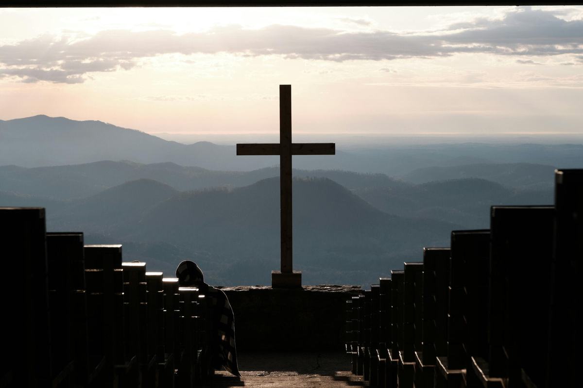 A cross on a hilltop overlooking mountain ridges at sunrise