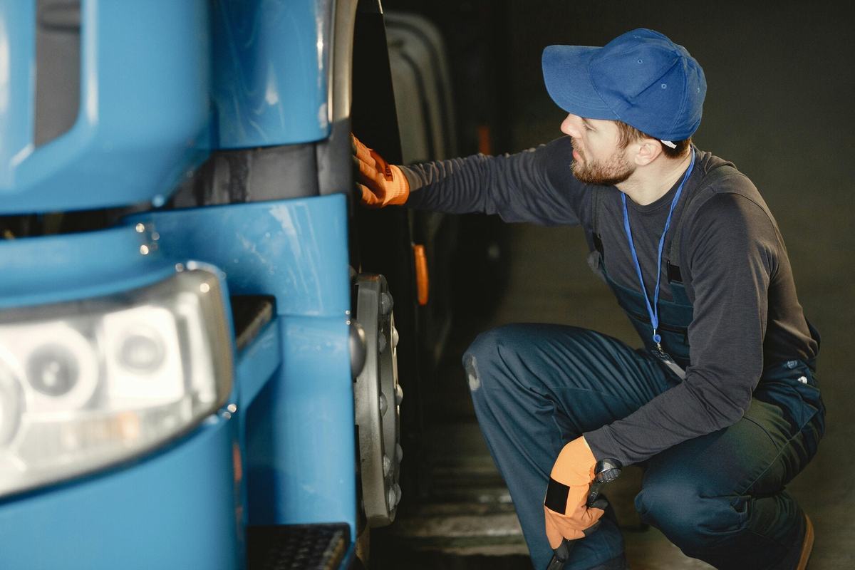 Technician crouched at the front wheel of a blue truck, checking the hub